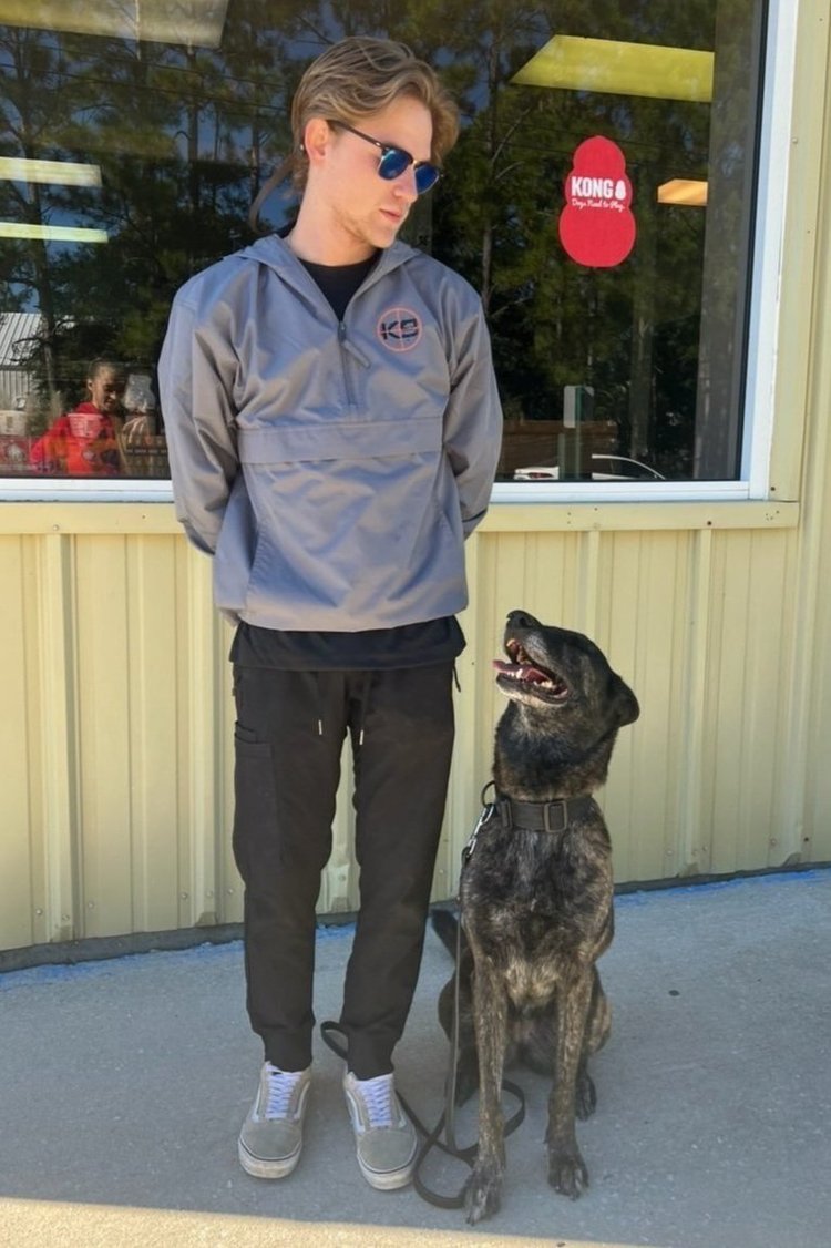 Tanner Kotowske standing outside the store with a brindle dog sitting at his side